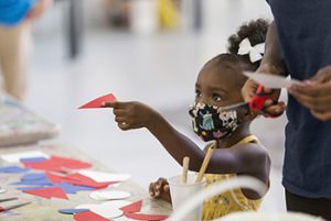 A little girl with a mask helps with the mural