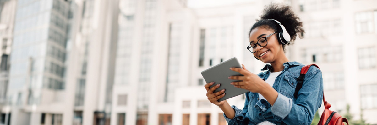 A smiling woman looking at her tablet wearing headphones