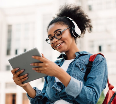 A smiling woman looking at her tablet wearing headphones